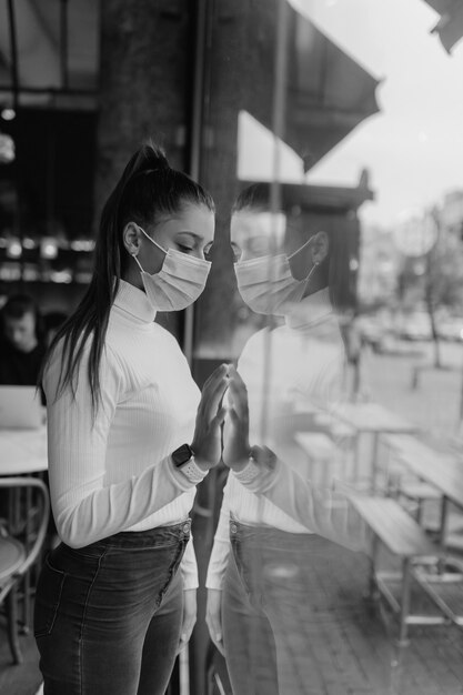 카페에서 창 앞에 서있는 얼굴 마스크에 젊은 여자
