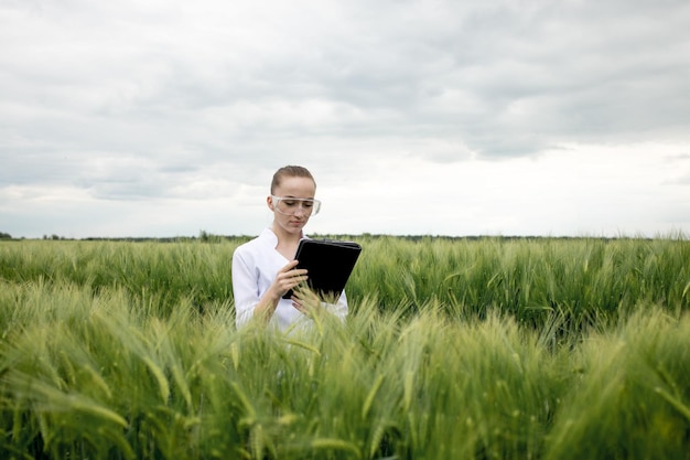 Молодая женщина-фермер в белом халате проверяет прогресс урожая на планшете у зеленой точилки