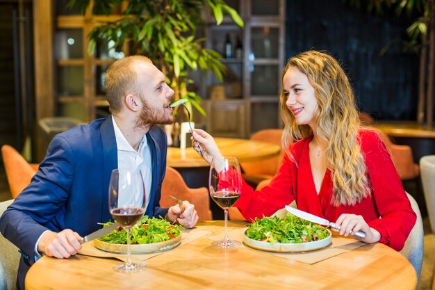 Young woman feeding man with salad in restaurant