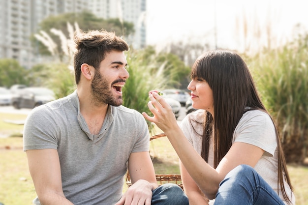 Young woman feeding strawberry to her boyfriend in the park