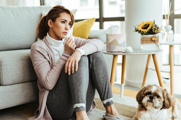 Young woman feeling sad and using tissues while sitting on the floor at her home