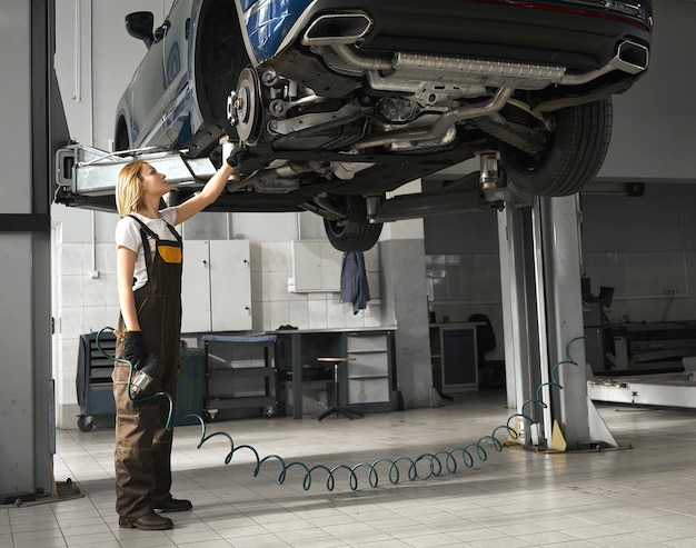 Young woman female mechanic checking chassis in workshop