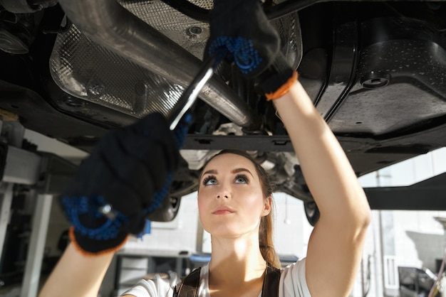 Young woman fixing undercarriage with wrench.