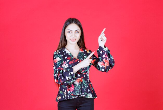 Young woman in floral shirt standing on red wall and showing upside