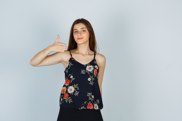 Young woman in floral top showing thumb up and looking happy