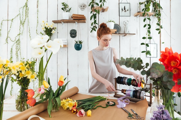 Young woman florist making bouquet with flowers and ribbons