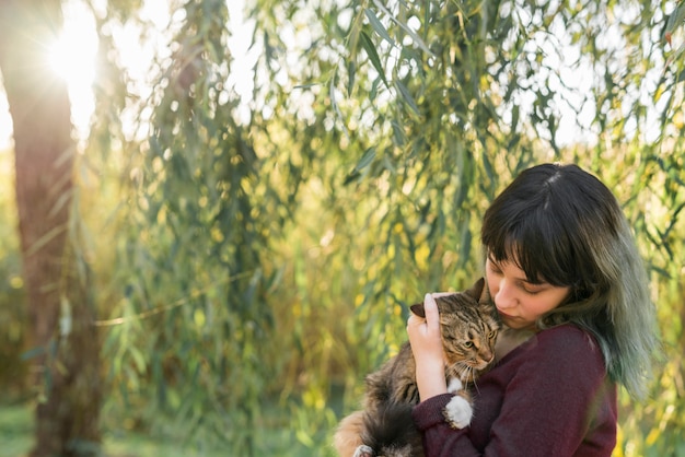 彼女の素敵なぶち猫を保持している森の若い女性