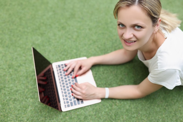 Young woman freelancer with laptop lies on green cover