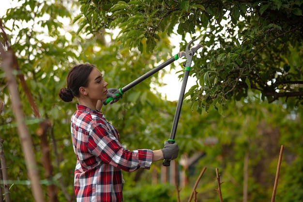Бесплатное фото Молодая женщина-гаденер срезает ветки на дереве, заботясь о природе, хобби-саде