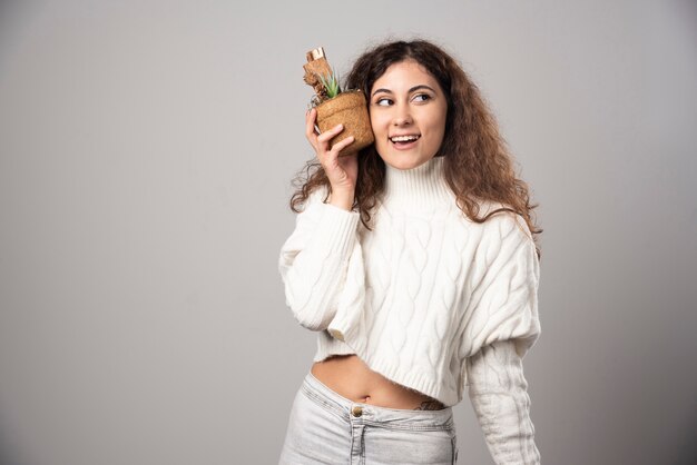 Садовник молодой женщины, держа растение на серой стене. Фото высокого качества