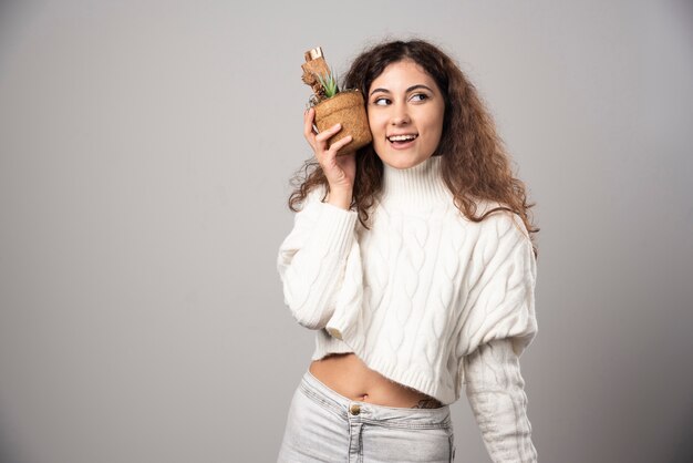 灰色の壁に植物を保持している若い女性の庭師。高品質の写真