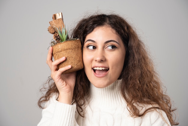 Young woman gardener holding a plant on a gray wall. High quality photo