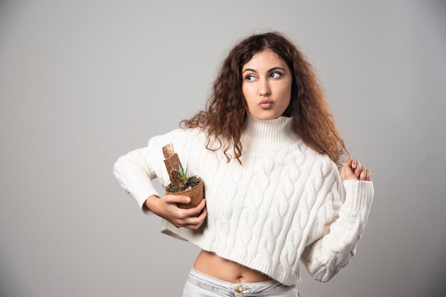 Young woman gardener holding a plant on a gray wall. High quality photo