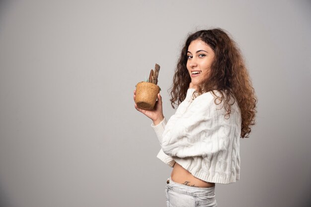 Young woman gardener holding a plant on a gray wall. High quality photo