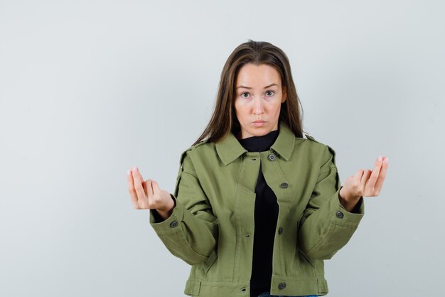 Young woman gesturing like explaining something in green jacket front view.