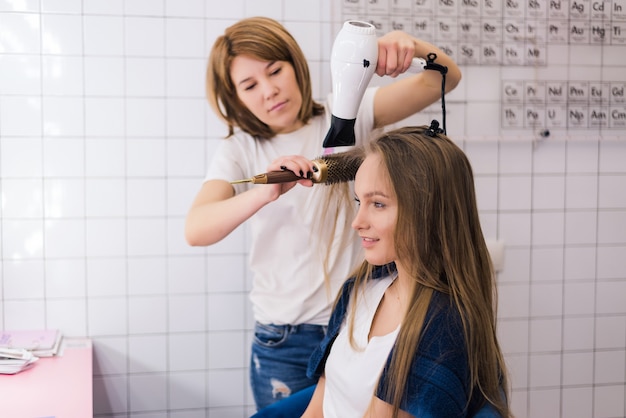 Free photo young woman getting new hairstyle with dryer at professional hair styling saloon.