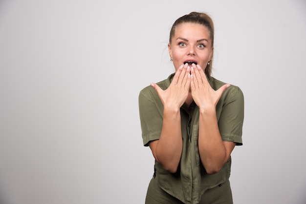 Young woman getting surprised on gray wall.