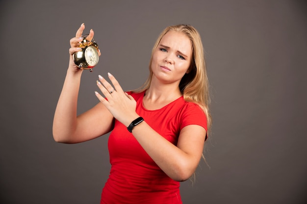 Young woman getting tired with clock on dark wall. 