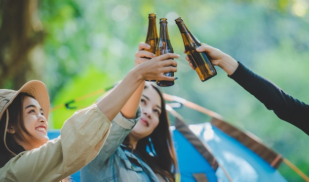 テントのキャンプチェアでリラックスした若い女性とガールフレンドの旅行者彼らは一緒に楽しく幸せに話しているキャンプ中に応援し、ビールを飲んでいます