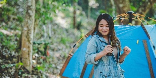 Young woman and girl friends travelers relaxing in camp chairs at tent They are cheering and drinking beer during camping talking with fun and happy together