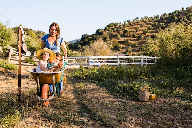 Young woman giving mother and daughter a ride in wheelbarrow at field