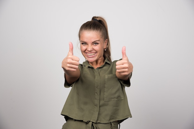 Free photo young woman giving thumbs up on gray wall.