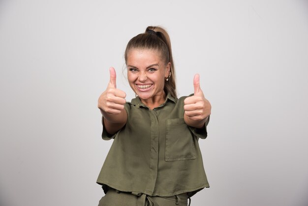 Young woman giving thumbs up on gray wall.