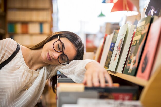 Young woman in glasses sleeping on books in library