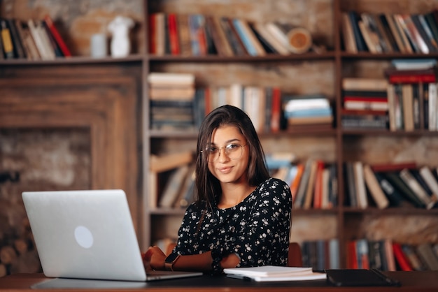 Young woman in glasses works at the laptop while sitting at table