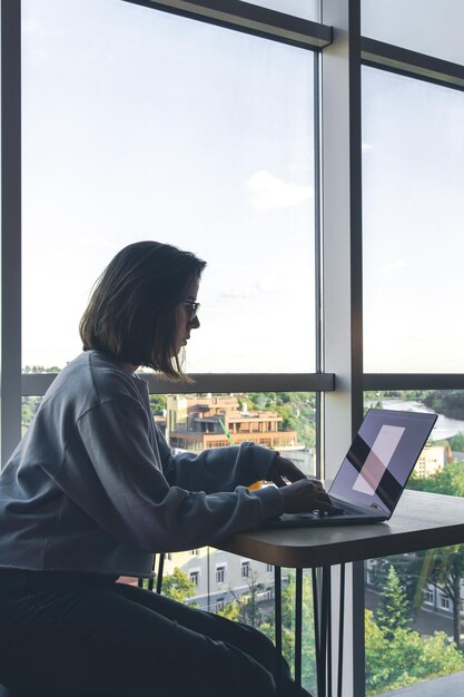 A young woman in glasses works behind a laptop at the workplace