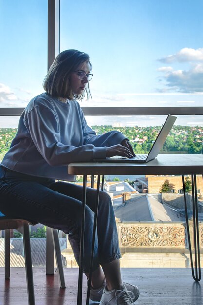 A young woman in glasses works behind a laptop at the workplace