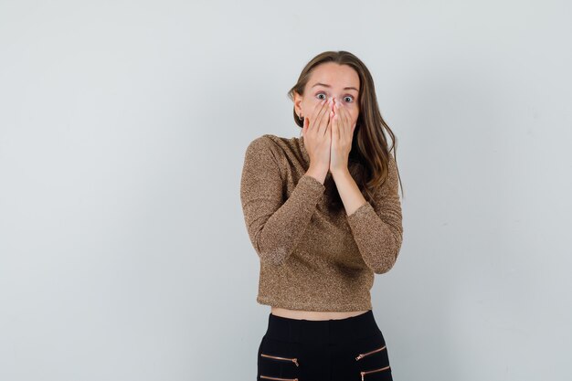 Young woman in golden blouse holding hands on her mouth