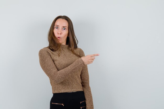 Young woman in golden blouse pointing aside and looking weird