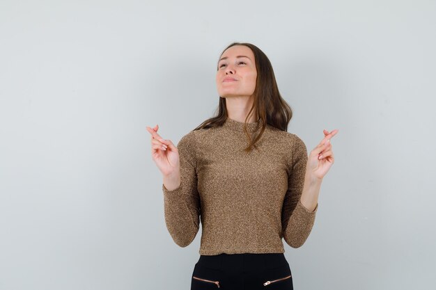 Young woman in golden blouse showing her crossed fingers while looking away and looking confident