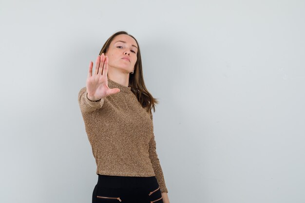 Young woman in golden blouse showing stop gesture and looking strict