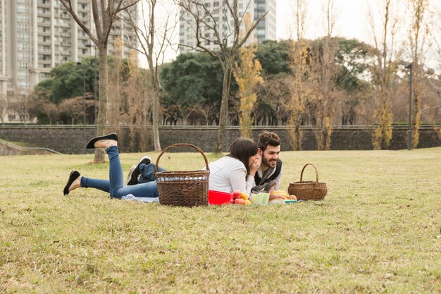 公園の毛布に横たわっているボーイフレンドの耳にゴシップする若い女性