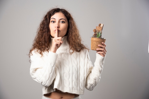 植木鉢を取る灰色の背景の上の若い女性。高品質の写真