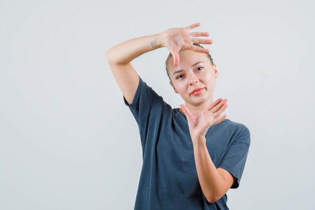 写真を撮ったり、陽気に見えるように手のひらを上げる灰色のTシャツの若い女性