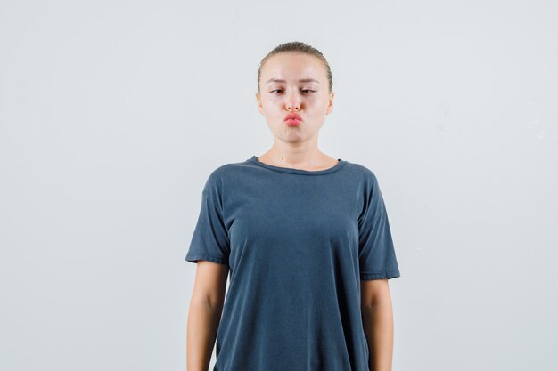 Young woman in gray t-shirt squinting eyes with folded lips and looking funny