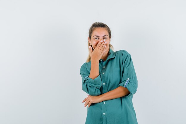 Young woman in green blouse covering mouth with hand while laughing and looking cute