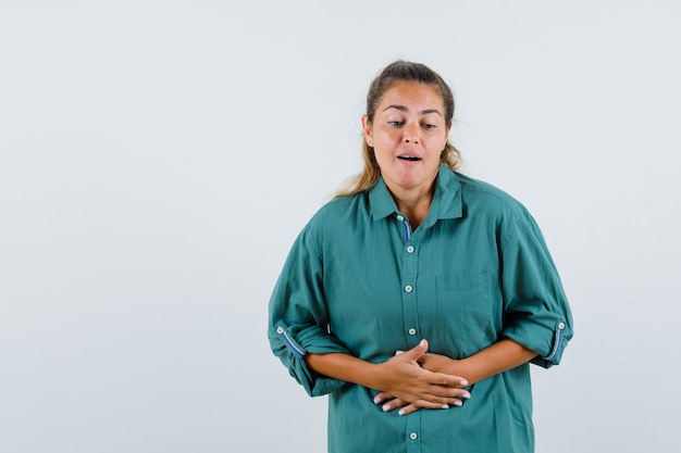 Молодая женщина в зеленой блузке с болит животом и выглядит измученной
