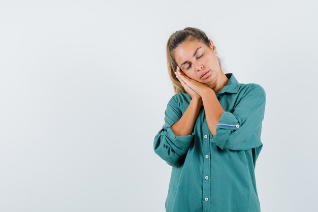 Young woman in green blouse leaning hands on cheek, trying to sleep and looking sleepy