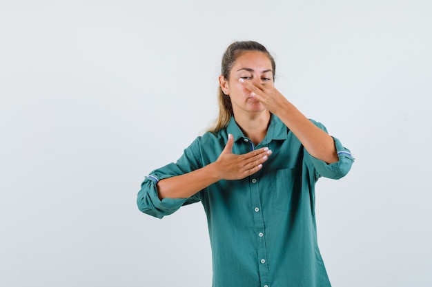 Young woman in green blouse pinching nose due to bad smell and looking annoyed