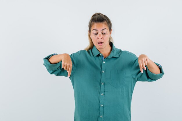 Young woman in green blouse pointing down with index fingers and looking cute