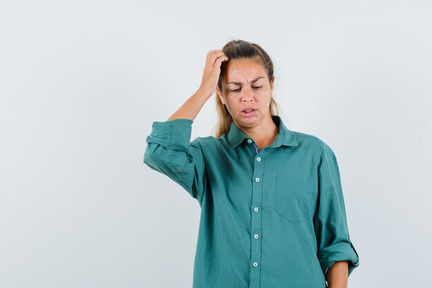 Young woman in green blouse scratching head and looking pensive