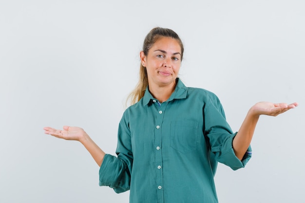 Young woman in green blouse shrugging shoulders and looking puzzled