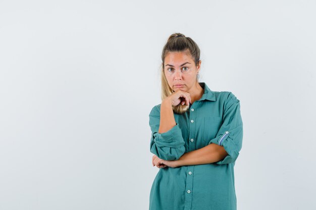 Young woman in green blouse standing in thinking pose and looking pensive