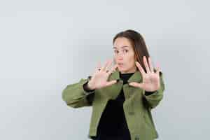 Free photo young woman in green jacket,black shirt showing stop gesture and looking worried , front view.