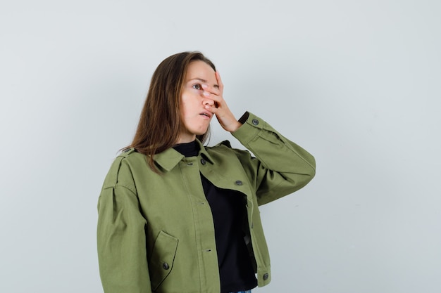 Free photo young woman in green jacket holding hand on face and looking troubled , front view.