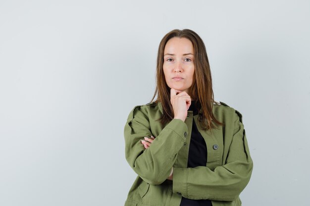 Young woman in green jacket listening someone and looking careful , front view.